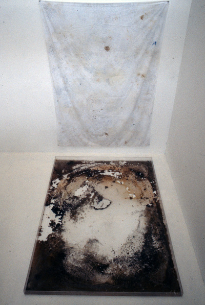 "Residue"  Sheet with various stains, plexiglass box with residue.  90" x 77" x 90"  1990s    This was a performed sculpture. I carried the sheet around with me for a couple of months, using it to absorb all stains created by my body, including food and writing.  Then I washed the sheet and poured the dirty water into a shallow plexiglass box the same size as the sheet.